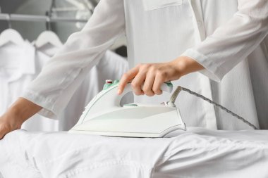 Evde beyaz gömlek ütüleyen kadın, yakın plan.