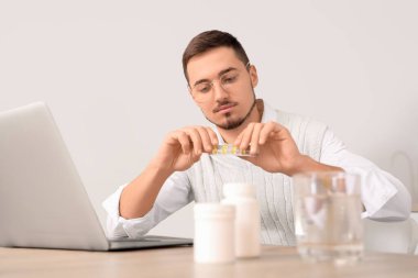 Bilgisayarlı genç adam evde hap alıyor.