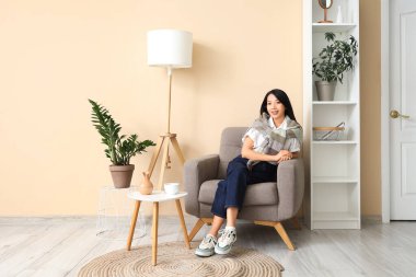 Young Asian woman sitting in armchair at home