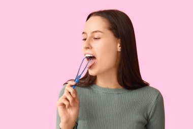 Pembe arka planda dil kazıyıcısı olan güzel genç bir kadın.