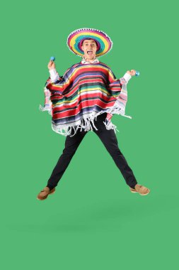 Yeşil arka planda zıplayan marakas şapkalı Meksikalı genç adam.