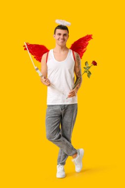 Aşk tanrısı gibi giyinmiş, sarı arka planda gül ve yay taşıyan genç bir adam. Sevgililer Günü kutlaması