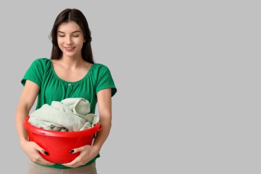 Gri arka planda temiz çamaşırları olan sepeti tutan genç bir kadın.