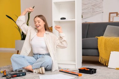 Güzel, genç ve mutlu bir kadın beyaz raf ünitesini evde monte ediyor.