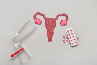 Gri arka planda doğum kontrol hapı ve jinekolojik spekulum içeren kağıt rahim.