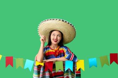 Meksikalı elbiseli mutlu bir genç kadın ve yeşil arka planda bir şeye bakan bir çelenk.