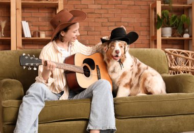 Güzel genç bir bayan, hoş bir Avustralyalı çoban köpeğiyle gitar çalıyor.