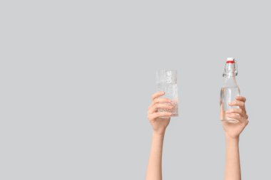 Şişeli kadın elleri ve gri arka planda bir bardak su.