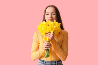 Beautiful young happy woman with bouquet of beautiful narcissus on pink background
