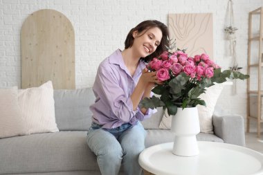 Young woman with pink roses in vase on table at home