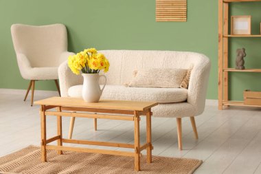 Oturma odasının içinde kanepe, sehpa ve sürahide nergis çiçekleri var.