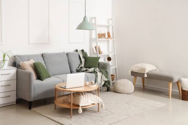 Modern interior of living room with grey sofa and laptop on table