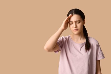 Bej arka planda baş ağrısı çeken güzel bir genç kadın.