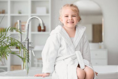 Evdeki küvette oturan bornozlu tatlı küçük kız.