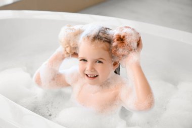 Küvette banyo süngerleriyle oynayan tatlı küçük kız.