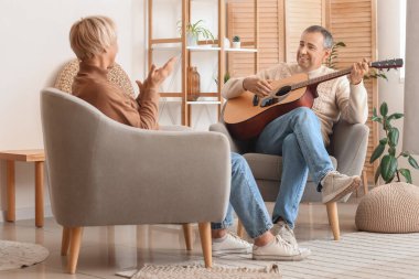 Gitarlı yaşlı adam evde karısına şarkı söylüyor.
