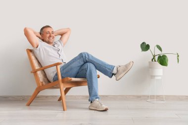 Yaşlı adam beyaz duvarın yanındaki koltukta dinleniyor.