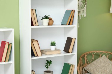 Odadaki yeşil duvarın yanındaki kitap rafında.