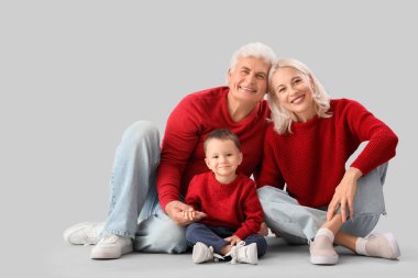 Gri arka planda sıcak kazaklar giyen mutlu büyükanneleri ve büyükbabaları olan sevimli küçük bir çocuk.