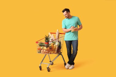 Sarı arka planda alışveriş arabası ve defteri olan mutlu genç bir adam.