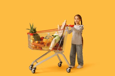 Sarı arka planda alışveriş arabası olan şirin, mutlu küçük kız.