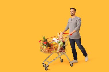 Sarı arka planda alışveriş arabası olan mutlu genç bir adam.