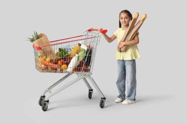 Mutluluk dolu alışveriş arabası ve gri arka planda ekmekleri olan sevimli küçük bir kız.