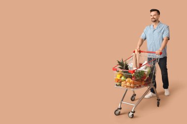 Bej arka planda alışveriş arabası olan mutlu genç bir adam.