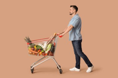 Bej arka planda alışveriş arabası olan mutlu genç bir adam.