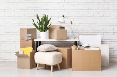 Beyaz tuğla duvarın yanında ev bitkisi ve karton kutularla dolu bir masa. Taşınma konsepti