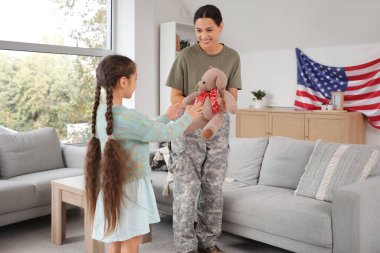 Evde kızına oyuncak ayı taşıyan kadın asker.