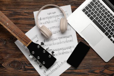 Bilgisayarlı müzik sayfaları, cep telefonu, kulaklık ve gitar ahşap arka planda.
