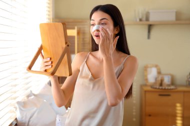 Yatak odasında burun bandı ve ayna olan genç bir kadın.