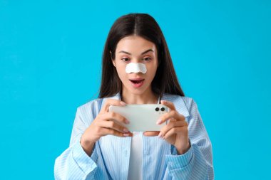 Young woman with nose patch taking selfie on blue background clipart