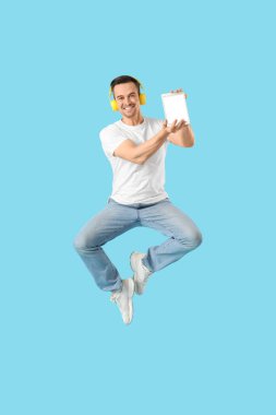 Mavi arka planda tablet bilgisayarı ve kulaklığı olan zıplayan adam. Tasarım için model