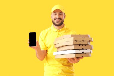 Sarı arka planda pizza kutuları ve telefonu olan erkek kurye.