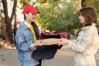 Bayan Asyalı kurye müşteriye dışarıda pizza ısmarlıyor.