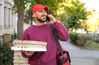Pizza kutuları olan erkek kurye dışarıda telefonla konuşuyor.