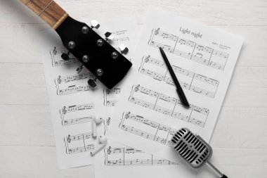Müzik kağıtları, kulaklıklar, gitar ve mikrofon beyaz ahşap arka planda