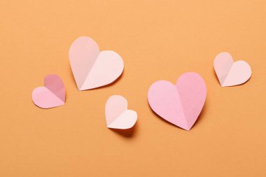Turuncu zemin üzerinde pembe kağıt kalpler olan kompozisyon. Sevgililer Günü kutlaması