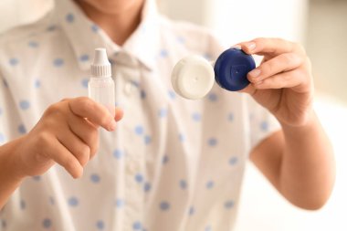 Kontak lens kutusu olan küçük bir kız ve banyoda bir şişe solüsyon, yakın plan.