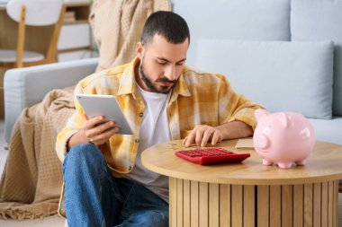 Evde para sayan tabletli stresli bir genç adam.