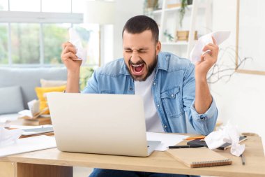 Evinde kağıt kırıntıları olan stresli bir genç adam bağırıyor.