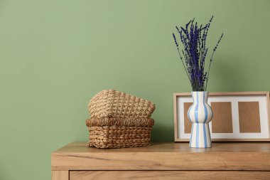 İçinde lavanta çiçekleri, çerçeve ve sepetler olan vazo yeşil duvarın yanında.