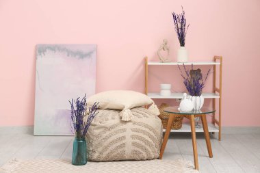 İçinde pouf, raf ünitesi ve vazolarda lavanta çiçekleri olan oturma odası.