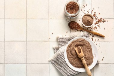 Beyaz fayans zemininde tohumlu keten unu ve kavanoz.