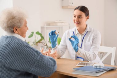 Klinikteki yaşlı kadına işitme cihazı gösteren kadın doktor.