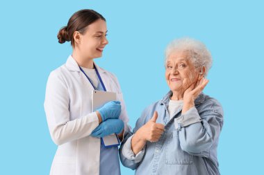 İşitme cihazı ve mavi arka planda doktor olan yaşlı bir kadın.