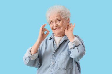 İşitme cihazı olan yaşlı bir kadın mavi arka planda iyi görünüyor.