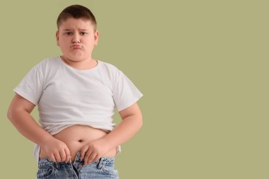 Şişman çocuk yeşil arka plandaki dar kotları iliklemeye çalışıyor. Diyet kavramı